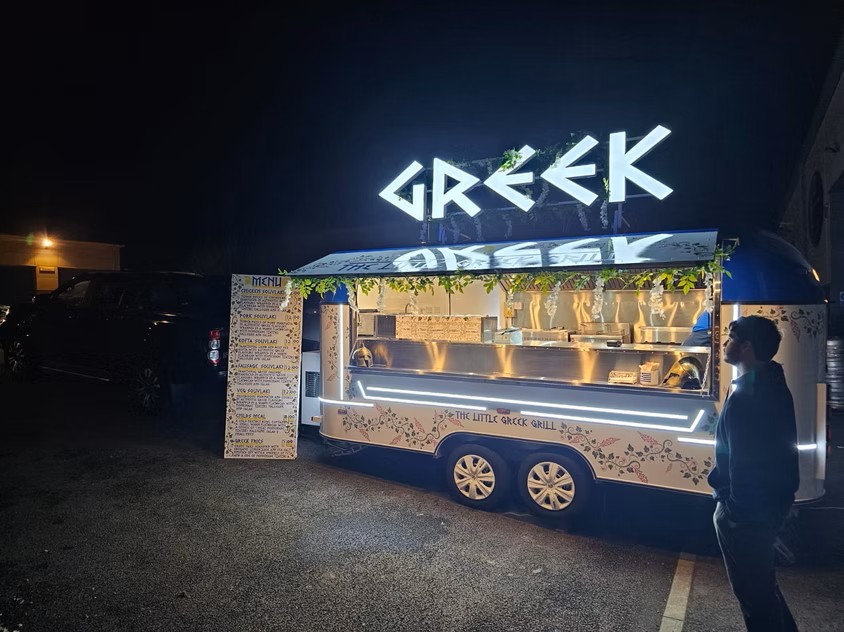 Food trailer with 'GREEK' illuminated 3D sign at night