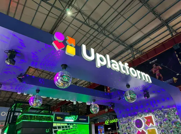 Face-lit 3D sign for Uplatform with glowing white letters and colorful cube-like icons above a vibrant expo booth.