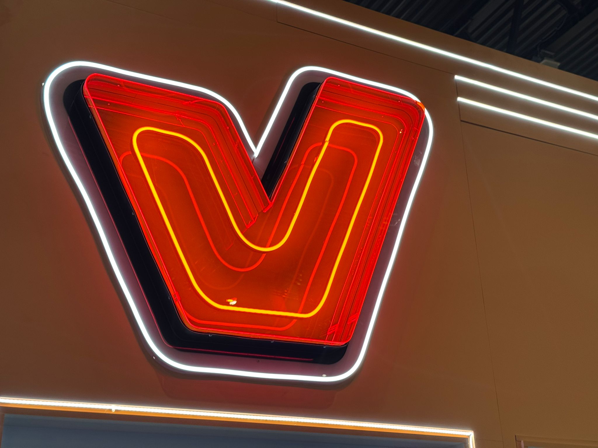 Layered red neon-style V sign with glowing white LED outline mounted on a wall.